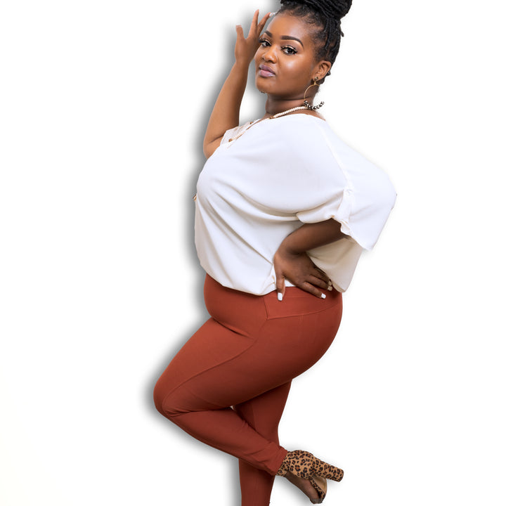 model posing on white background wearing rust colored scuba high waist pull on pants paired with a tucked white top and leopard shoes